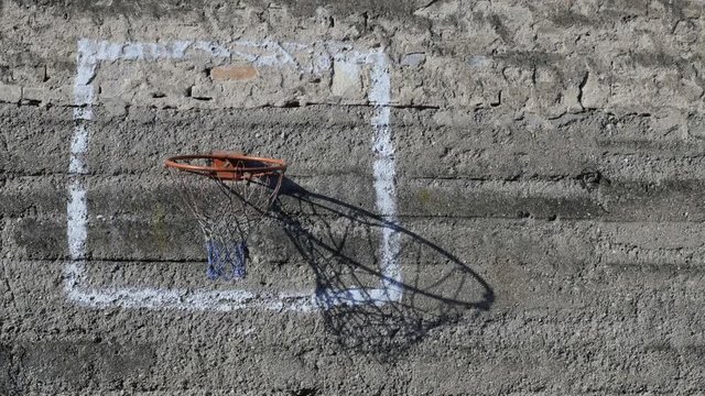 Shadows from basketball ring are sliding on the surface of the rough concrete wall