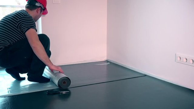 professional worker man laying underlay for laminate flooring installation