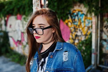 Stylish casual hipster girl in jeans wear and glasses against large graffiti wall.