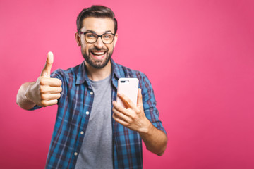 Fototapeta premium Portret wesoły brodaty mężczyzna biorąc selfie i pokazując kciuki do góry gest na różowym tle. Odosobniony.