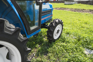 A small mini blue tractor stands on a farm yard on green grass and waits for work to begin.