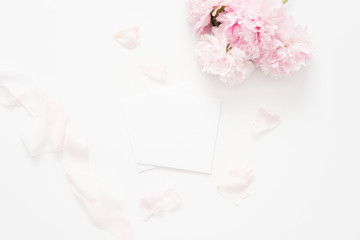 Obraz premium Elegant feminine wedding or birthday flat lay composition with pink peonies floral bouquet and silk ribbon. Blank paper card, mockup, invitations. Flatlay, top view.