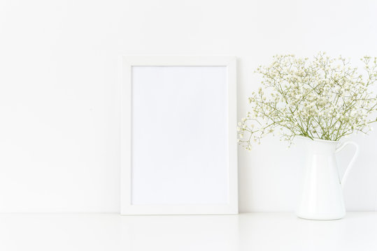 White frame mockup A4 in interior. Frame mock up background for poster or photo frame for bloggers, social media, lettering, art and design. Indoor, frame on table with flowers in jug, stationary.