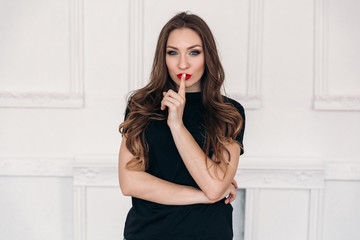 A young beautiful girl on a white background wearing a black T-shirt with red lips, has long dark...