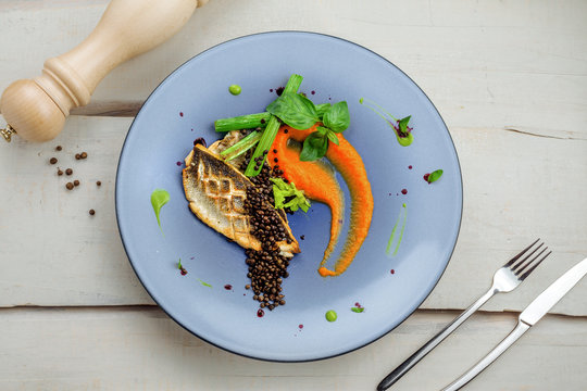 Grilled seabass fish fillet steak with vegetables on a plate. Healthy gourmet seafood meal on a table. Directly above top view shot.
