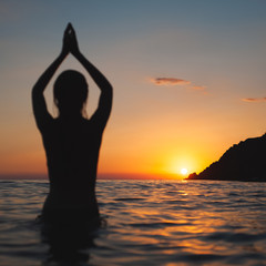 Fototapeta premium yoga pose woman sunset silhouette in sea. Ocean bathing at dawn