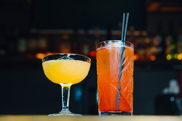 two cocktails at bar counter. orange red and yellow drinks