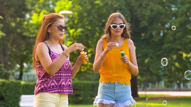 leisure and friendship concept - happy teenage girls or friends blowing bubbles in summer park