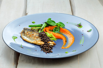 Seabass fish fillet stake cooked on a grill with healthy vegetables on a plate. Healthy seafood food on a   rustic wooden table. Close-up shot.