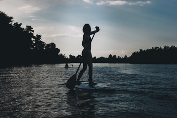 silhouette of athletic woman standup paddleboarding on river