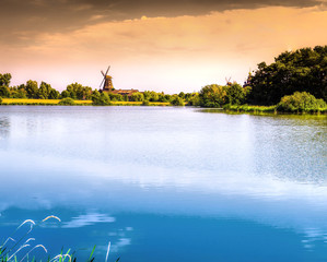 Pond area with open space, shore at the background with trees, forest and a mill
