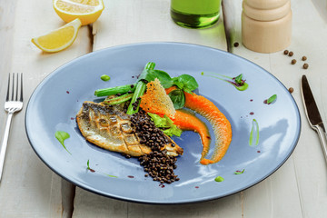 Gourmet grilled seabass fish fillet steak and vegetable salad. Delicious healthy meal made of seafood and vegetables on a rustic table.