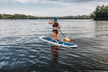 beautiful athletic tattooed woman in bikini paddle boarding on river