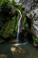 Fototapeta na wymiar Cascada que cae sobre un río con una roca en el Nacedero del Urederra
