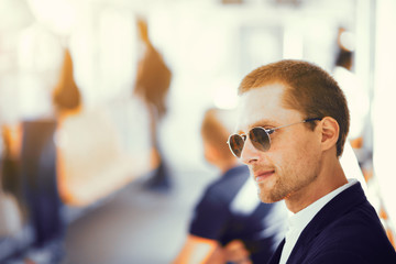 Businessman in metro. Handsome man in suit and sunglasses sitting on subway train. People blurred in background.