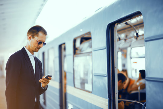 Businessman Checking His Phone Before Getting On Subway. Elegant Man Wearing Formal Clothes For Business Meeting Standing In Front Of Metro Train Texting Via His Phone.