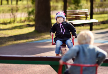 Little girl and boy having fun with carousel on outdoor playground