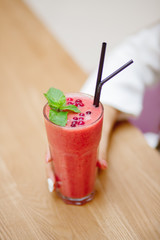 Young woman is holding useful smoothie from fresh berries and fruits in cafe.