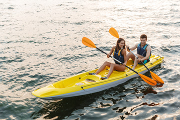 Loving couple kayaking on lake sea in boat - obrazy, fototapety, plakaty