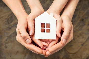 Hands holding house model on white wooden background