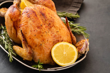 Roasted chicken with rosemary served on a metal plate with lemon on black table. Christmas turkey. Copy space.