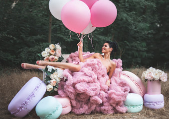 Fashion sexy woman dressed in pink stunning dress surrounded of French Macarons