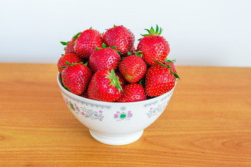 Fresh strawberries in bowl on wooden table.