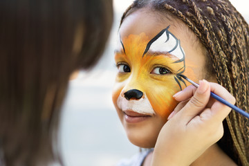 Little girl getting her face painted by face painting artist.
