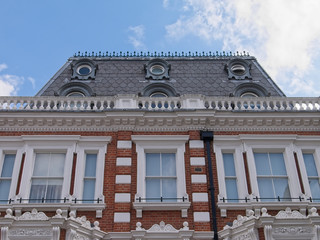 Details of Victorian townhouse exterior in London. Steep pitch terracotta tiled roof, cast iron railings, balustrade, sash windows and striped stonework. © DK Photography
