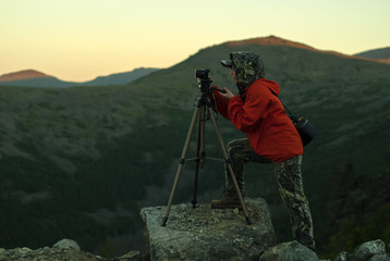 woman photographer takes a picture of a dawn in the mountains by camera on a tripod