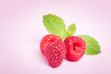 Raw ripe raspberries with fresh green mint leaf isolated on pink pastel background.