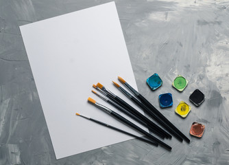 Painting brusches, white paper and watercolors on gray concrete background