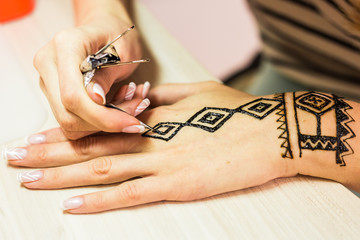 young woman mehendi artist painting henna on the hand.