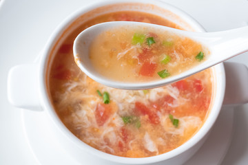 Traditional Chinese soup with tomatoes and egg in a white spoon on the background of a plate. Shallow depth of field.