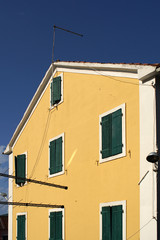 Old traditional yellow painted building with green wooden window covers