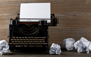 Vintage typewriter with empty, blank sheet of paper and crumbled paper balls on wood table