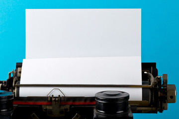 Close up of vintage typewriter with empty, blank sheet of paper on cyan