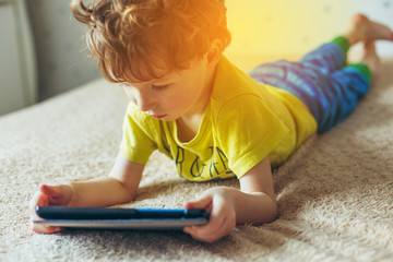 Little cute boy in a green T-shirt playing games on a tablet and watching cartoons. addiction concept