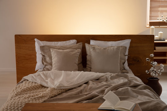 Book on cabinet in front of bed with cushions and sheets in bedroom interior with light. Real photo