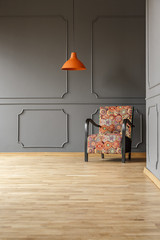 Dark grey sitting room interior with colorful pattern armchair and orange lamp in real photo with...