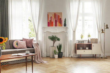 Drapes at windows and poster in white living room interior with couch and cupboard. Real photo