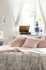 Pink pillows on bed in bright feminine bedroom interior with poster and window. Real photo