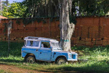 An old blue 4x4 stands under a gigantic tropical tree, Barichara/ Colombia/ South America