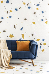Orange cushion and blanket on blue sofa in colorful living room interior with wallpaper. Real photo