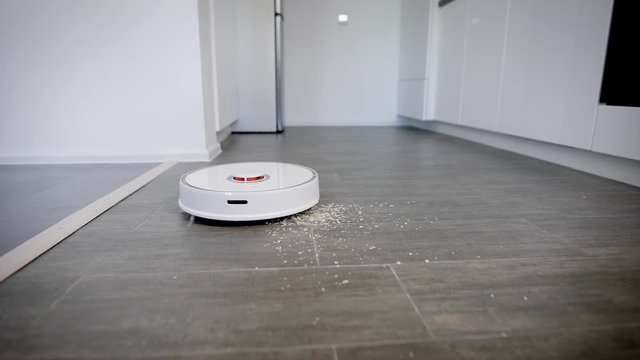 Close up shot of a robot vacuum cleaner cleaning kitchen parquet from crumbs and dust.