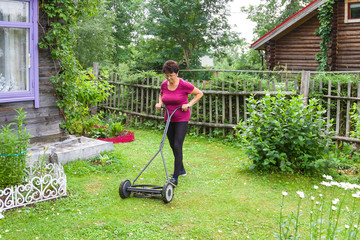 Garden work. Ederly woman mowing grass with lawn mower in the garden