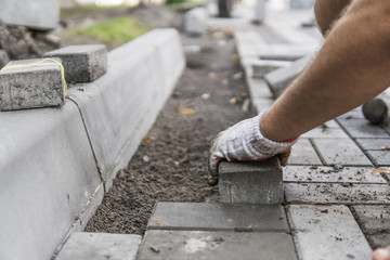 Hands of a builder in his orange gloved hands with a hammer fitting laying new exterior paving...