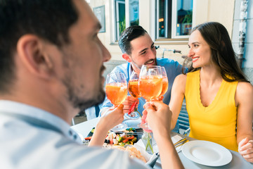 Four friends holding stemmed wine glasses while toasting together with a cold refreshing alcoholic drink during a delicious lunch at the restaurant