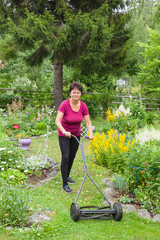 Garden work. Positive senior woman mowing grass with lawn mower in the garden