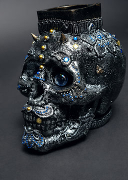 Skull decorated with colorful stones with candle on black background